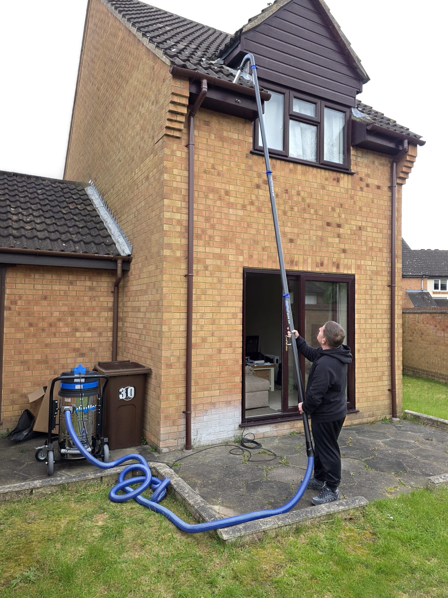 Engineer using a high-reach gutter vacuum system to clear blocked guttering on a two-storey home
